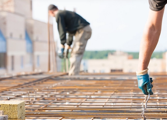 Deux artisans, portant des gants de sécurité, travaillent sur un coffrage en acier pour une dalle de béton. Leur précision et expertise garantissent une structure robuste et durable