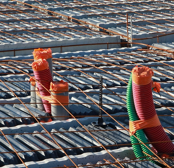 Installation de gaines techniques colorées sur une dalle de béton armé avec coffrage en acier. Les câbles et conduits sont sécurisés pour garantir une infrastructure fonctionnelle et durable