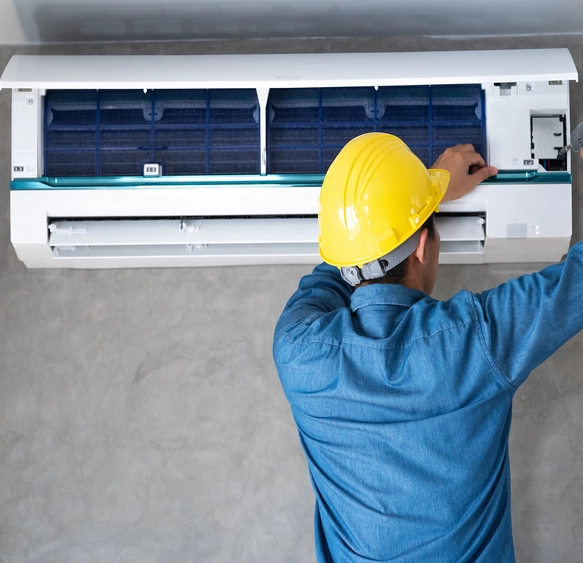 Technicien en casque jaune installe et ajuste un climatiseur mural. Son expertise garantit un fonctionnement optimal du système de climatisation dans un environnement résidentiel